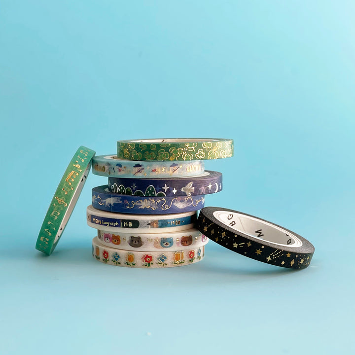 A stack of very thin washi tape rolls. Each roll has a different design and golden accents.