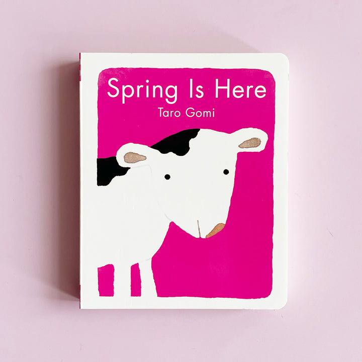 Bright pink board book with an illustration of a cow on the cover. The book  title is "spring is here"
