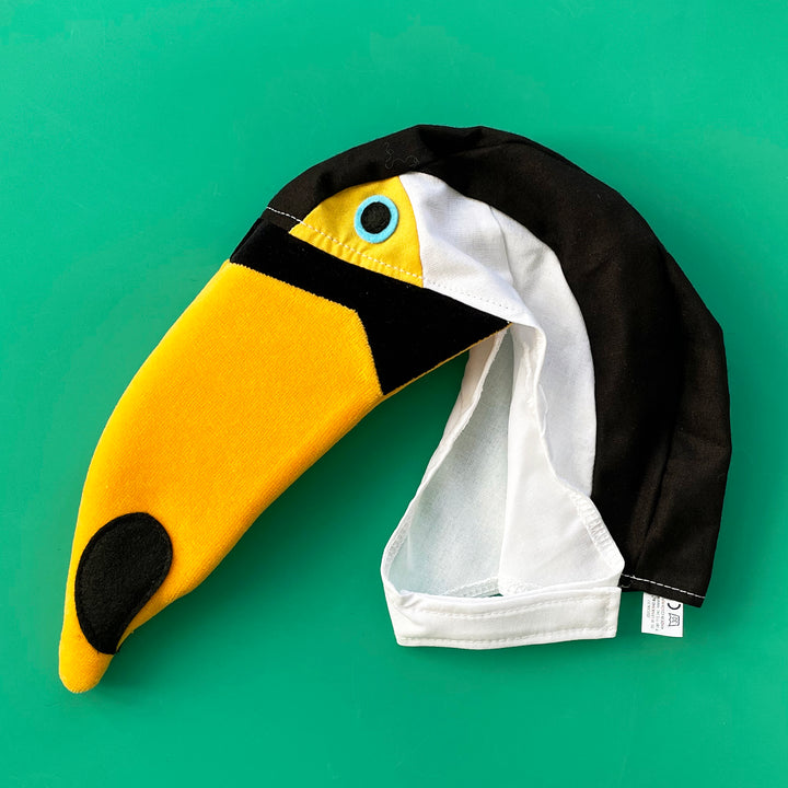 Black and white cotton toucan costume hat with long yellow cotton-velour beak and felt eyes.  Displayed on a bright green background.