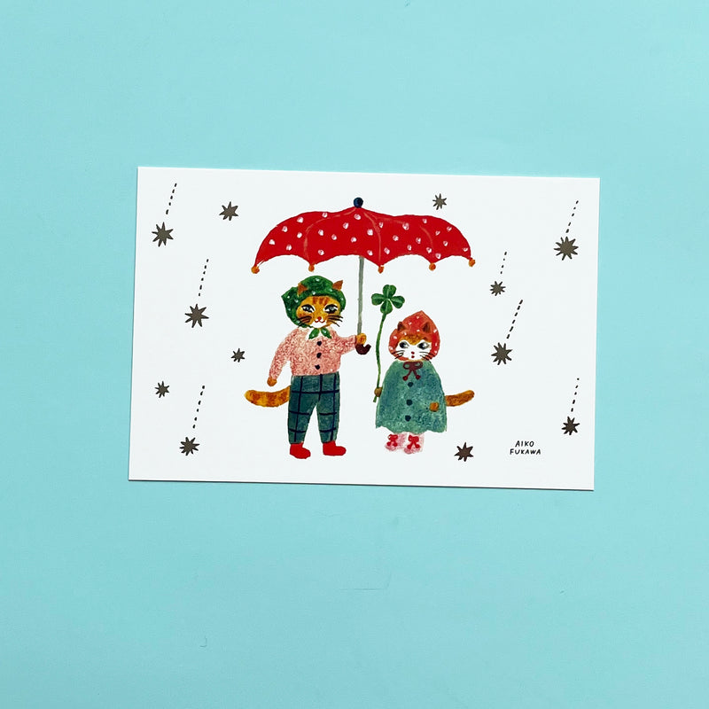 A post card with two anthropomorphic cats in outfits sharing a red umbrella as starts fall around them.