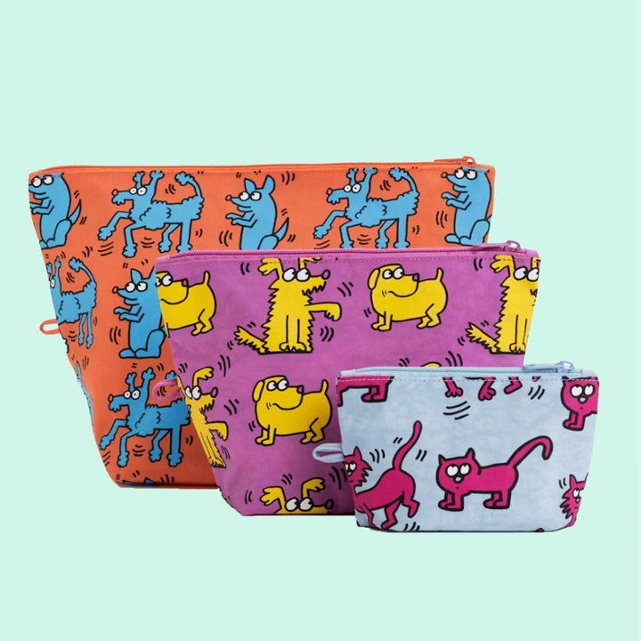 Three Keith Haring bags, orange, purple, and light blue with dog and cat illustrations on mint background.