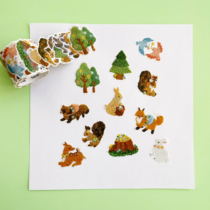 A roll of washi stickers featuring images of woodland animals in faux embroidered illustrations displayed on a light green background.