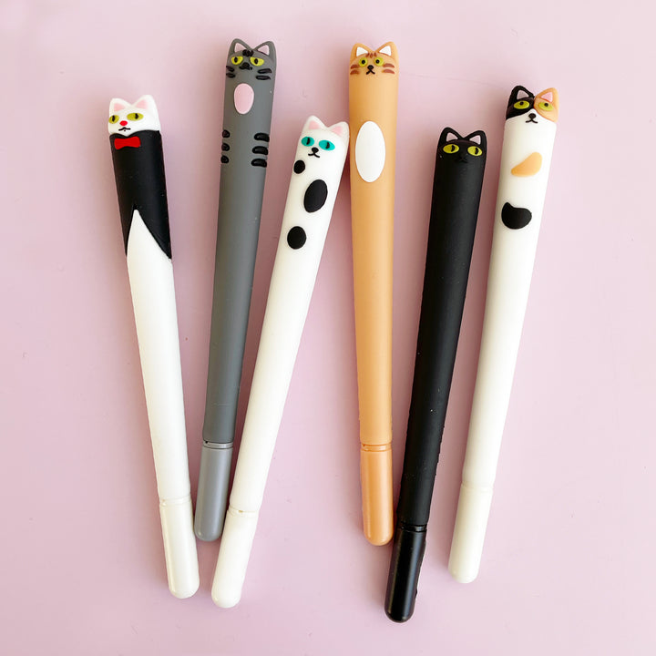 Seven cat shaped gel pens lying on a pink background.