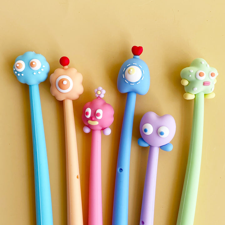 Six whimsical gel pens in various pastel colors on a yellow background.