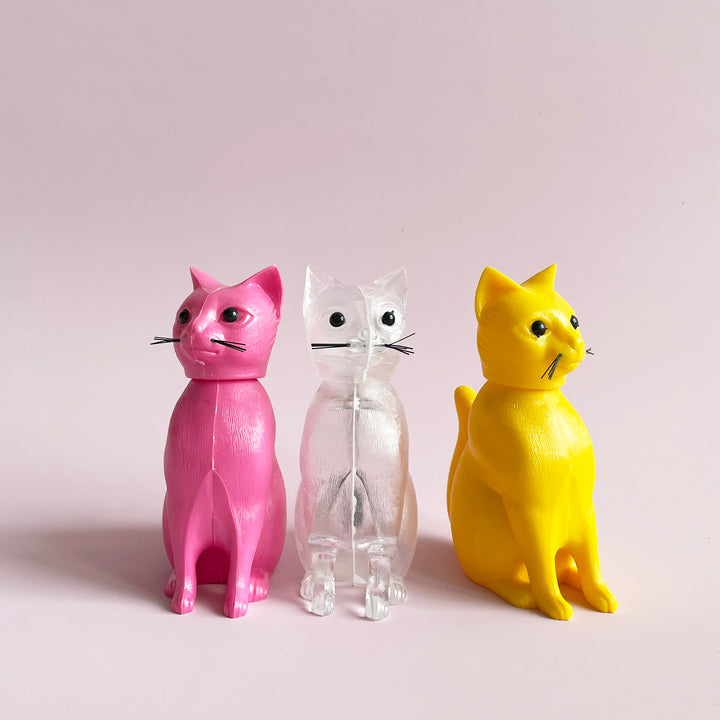 Three cat bobblehead figurines. They are pink, clear plastic, and yelllow