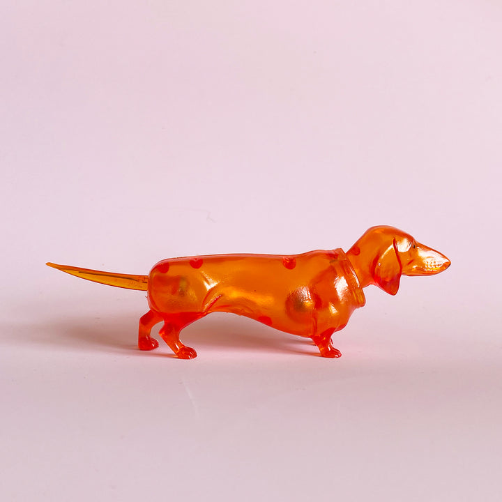 Translucent orange bobblehead figurine in profile on a light pink background
