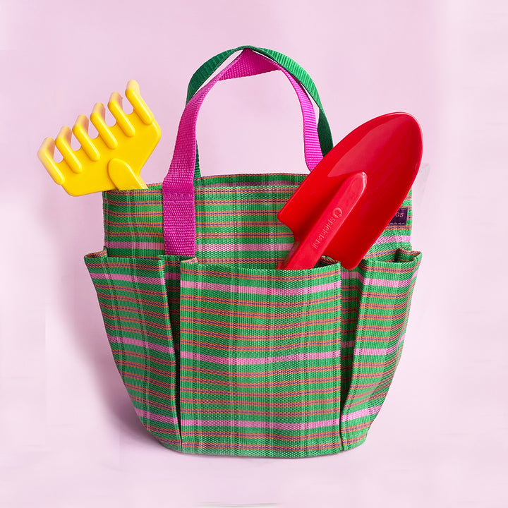A green and pink plastic mesh bag holding a yellow garden rake and red trowel