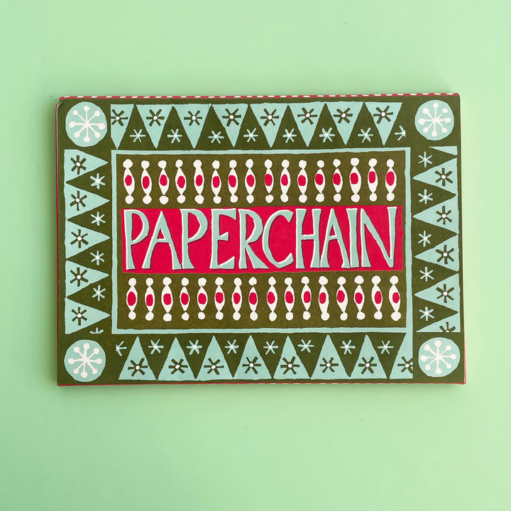 Colorful packaged for a DIY paperchain kit on a light green background. The package has hand-cut lettering and a hand-drawn graphic design.