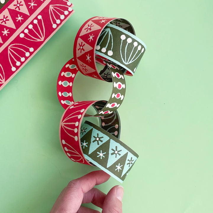 5 links of a DIY paper chain assembled and displayed on a light gree background. The chain has a graphic, hand-drwan pattern in shades of red and green.