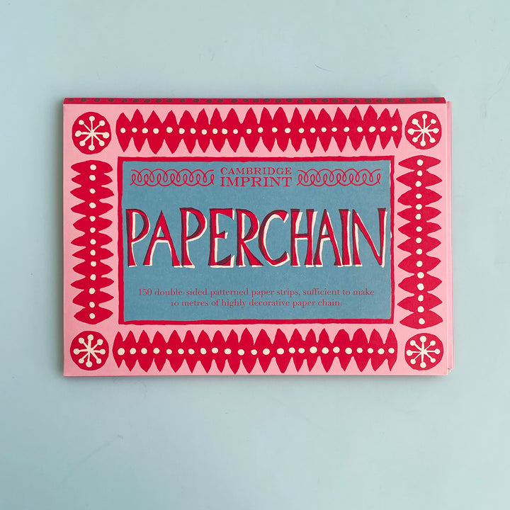 Package for a DIY paper chain on a light blue background. The package has hand-cut lettering and a hand-drawn graphic design in shades of red, pink and blue.