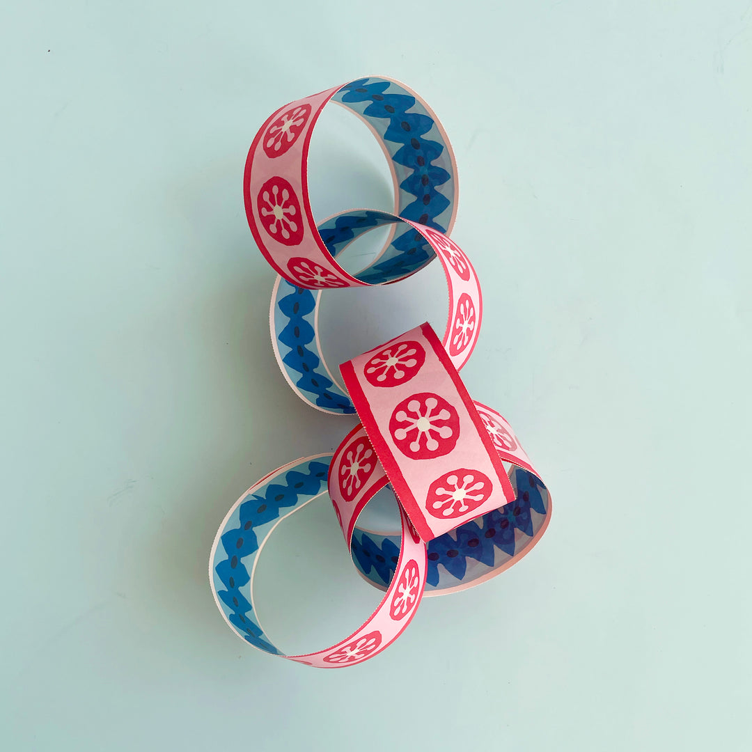 5 links of an assembles DIY paper chain displayed on a light blue background. The chain has a hand-drawn graphic design in shades of red, pink and blue.
