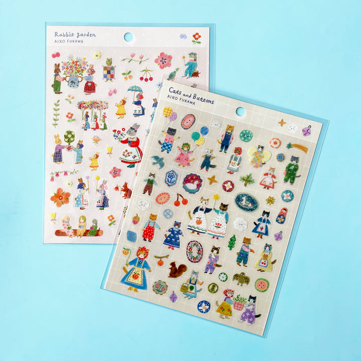 The "Cats and Buttons" and "Rabbit Garden" sticker sheets by Aiko Fukawa lay on a blue background.