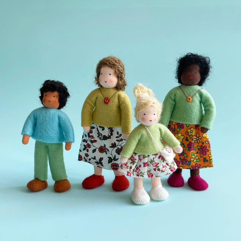 4 cotton dolls of various heights stand in a row. Three are wearing floral skirts, and one is wearing felt pants.