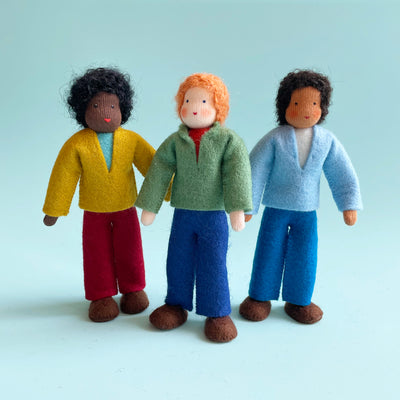 3 different 5.25-inch cotton dolls with felt outfits stand in a line next to each other. One doll has dark skin, black curly hair, a yellow shirt, and red pants. One doll has light skin, orange hair, a green shirt, and blue pants. The third doll has medium skin, dark hair, a light blue shirt, and blue pants.
