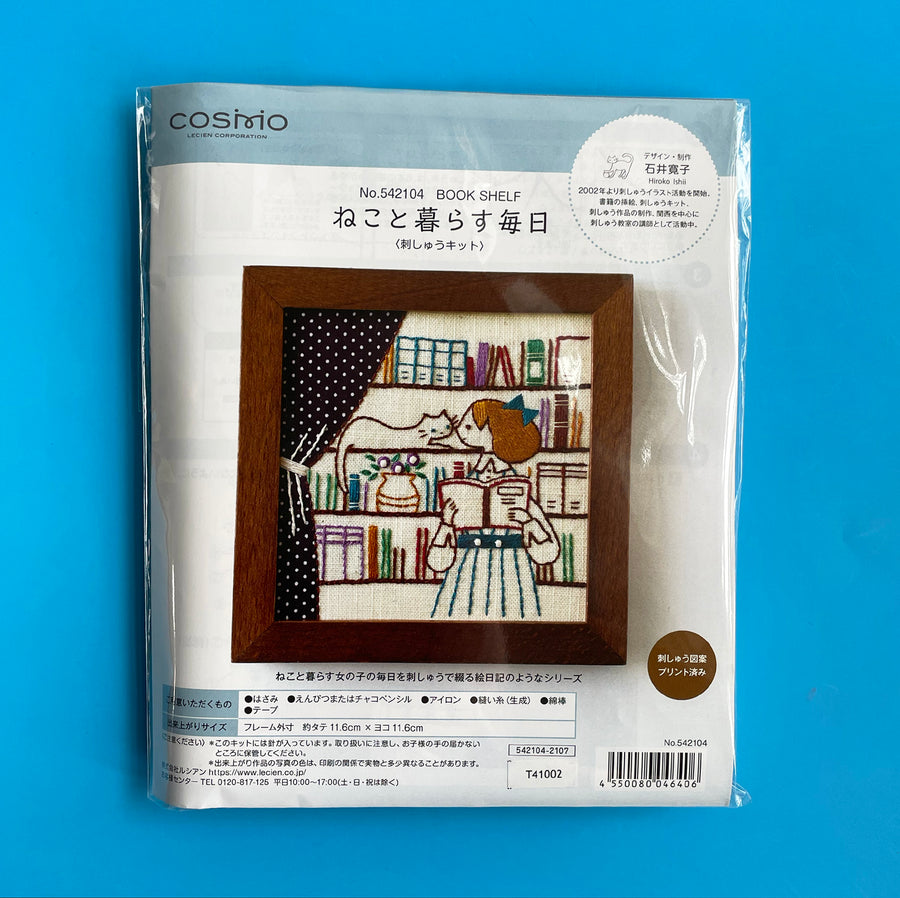 Packaged embroidery kit featuring an image of a girl reading a book against a book shelf filled with books, plants, and a cozy cat.