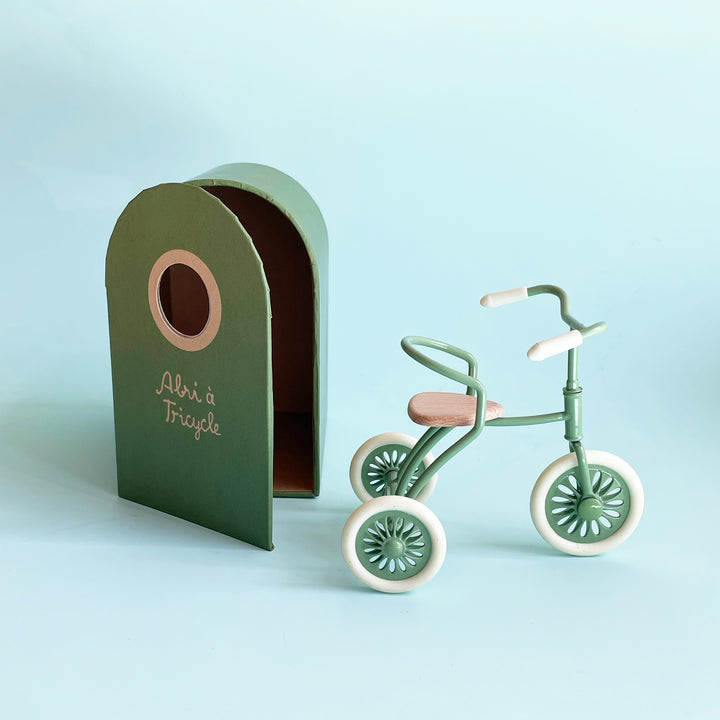 A miniature, vintage-style, mint-colored tricycle sits next to a green box with a curved top and open front.