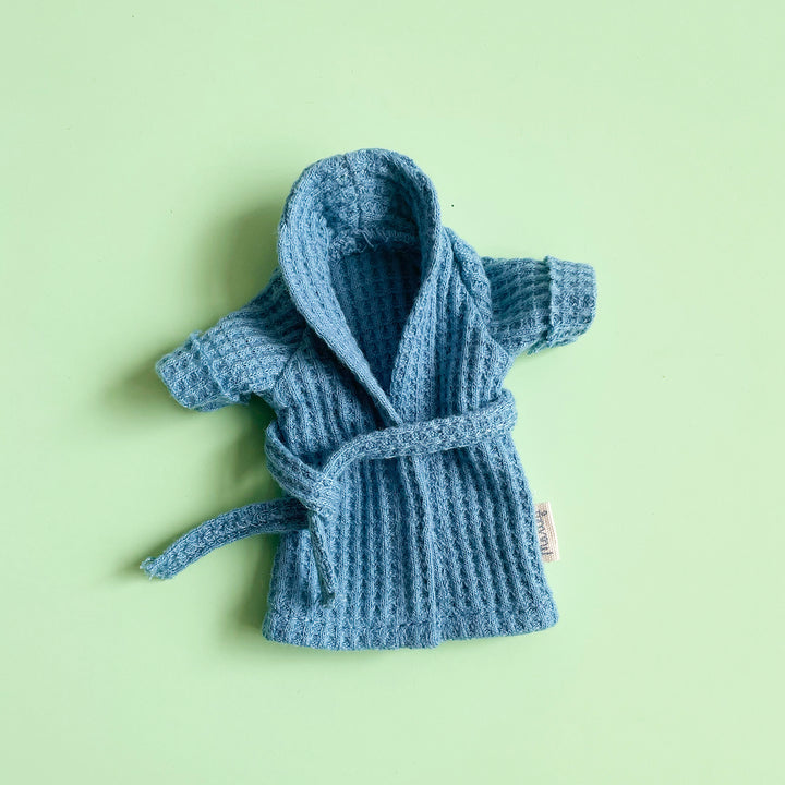 A miniature, blue, waffle-weave bathrobe laid flat on a light green background.