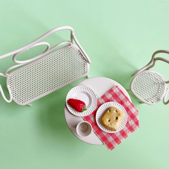Small white table with a muffin, strawberry, and teacup on a green background