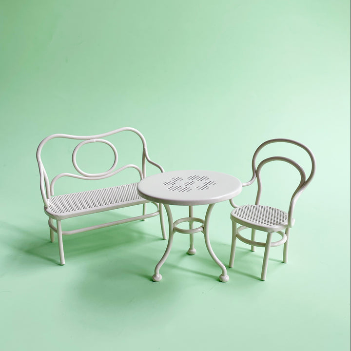 White metal dollhouse furniture set with a table and two chairs on a light green background