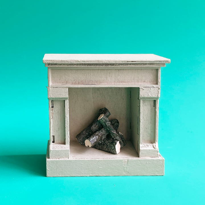 A miniature fireplace with distressed paint and realistic logs displayed against a bright green background.
