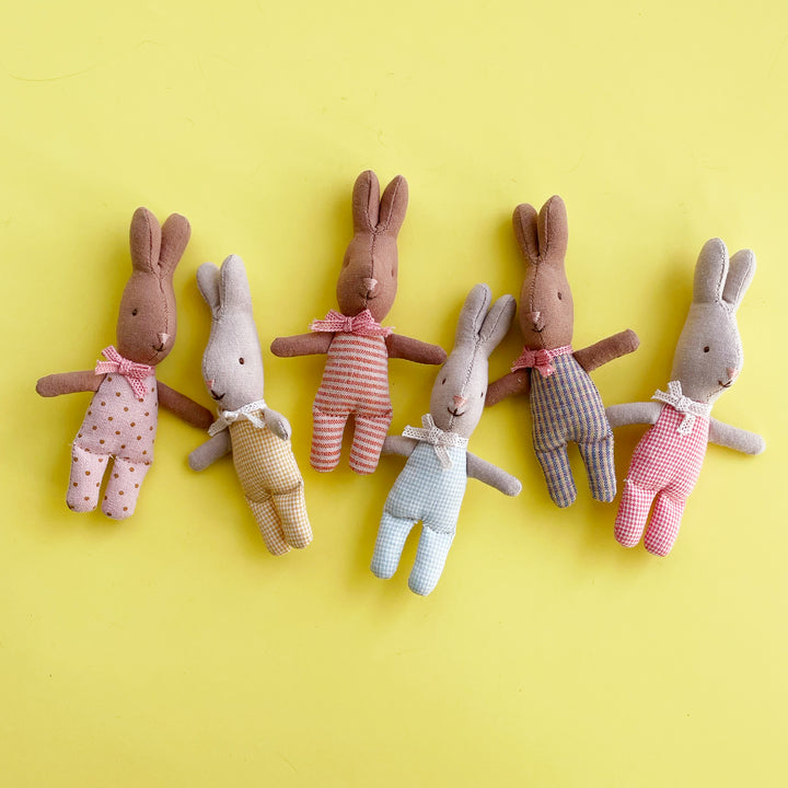 A row of six miniature cotton rabbits with colorful bodies are artfully scattered across a bright yellow background.