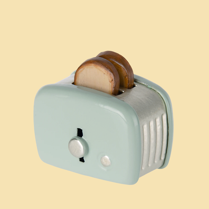 A small mint-colored metal toy toaster in a vintage style with two slices of bread sticking out the top.