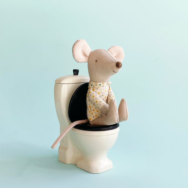 Little brother Maileg fabric mouse sitting o a tiny metal, black and white toilet on a light blue background.