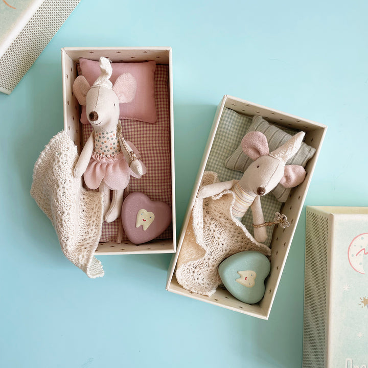 Two miniature fabric toy mice dressed as fairies in pastel colors, each nestled into their own boxes with checkered padding and knit blankets.