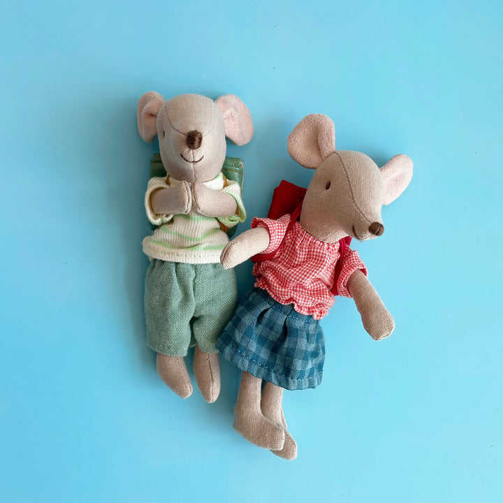 Two miniature, toy fabric mice dressed in colorful play clothes, snuggled together against a blue background.