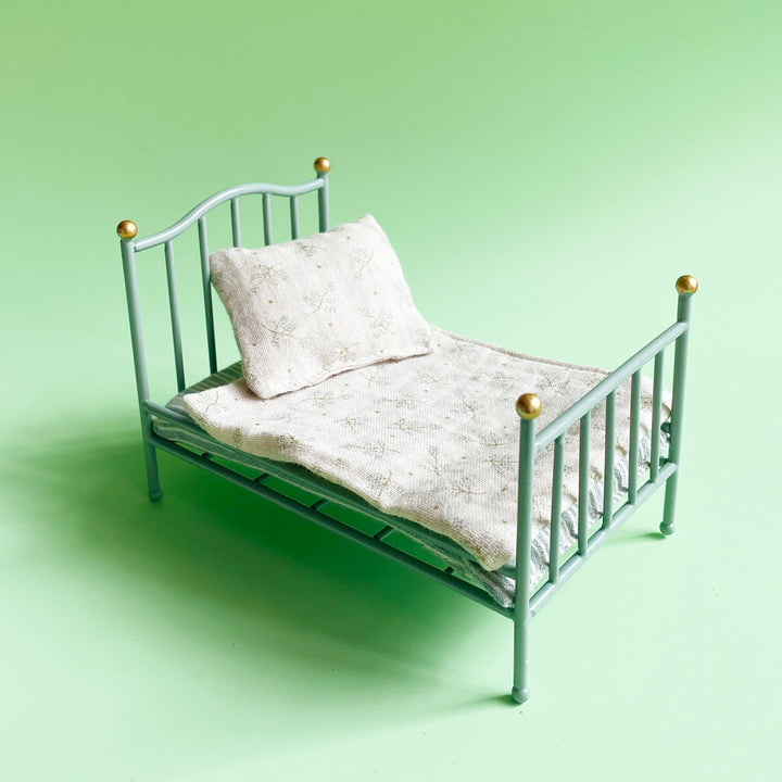 Miniature mint-colored, metal bed with floral print bedding on a light green background.
