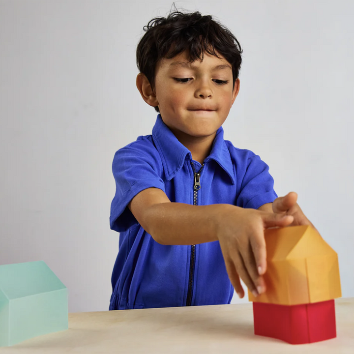 A young boy in a bright blue top carefully nesting a series of 3D paper houses inside one another.