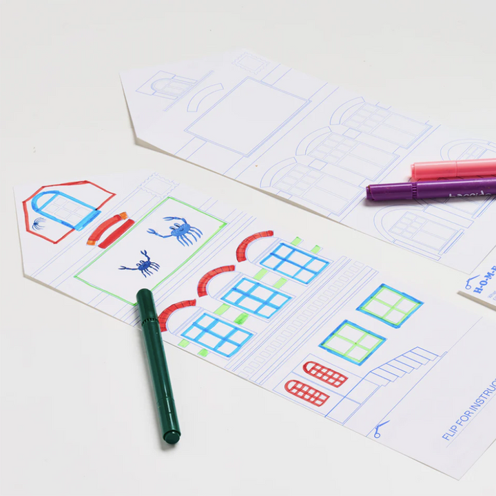 Process photo of a coloring activity from Majo Ideas Home Activity Kit. Includes two house-shaped coloring sheets with markers.