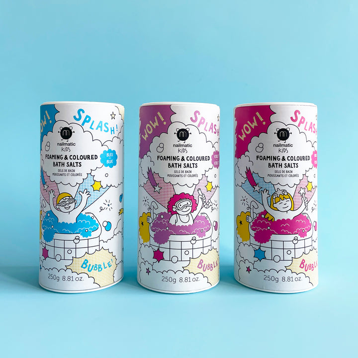 Three bottles of Nailmatic Foaming Colored Bath Salts on a light blue background. Packaging features cartoon drawings of kids playing in the tub with colorful bubbles.