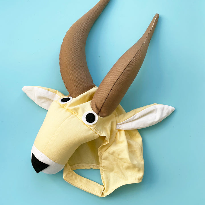 Yellow cotton antelope costume hat with large stuffed antlers, floppy ears, and felt eyes.  Displayed on a light blue background.