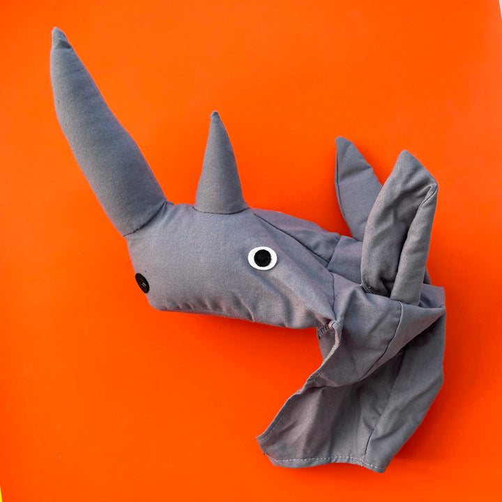 Grey cotton rhinoceros costume hat with stuffed snout and horn and felt eyes. Displayed on a bright orange background.