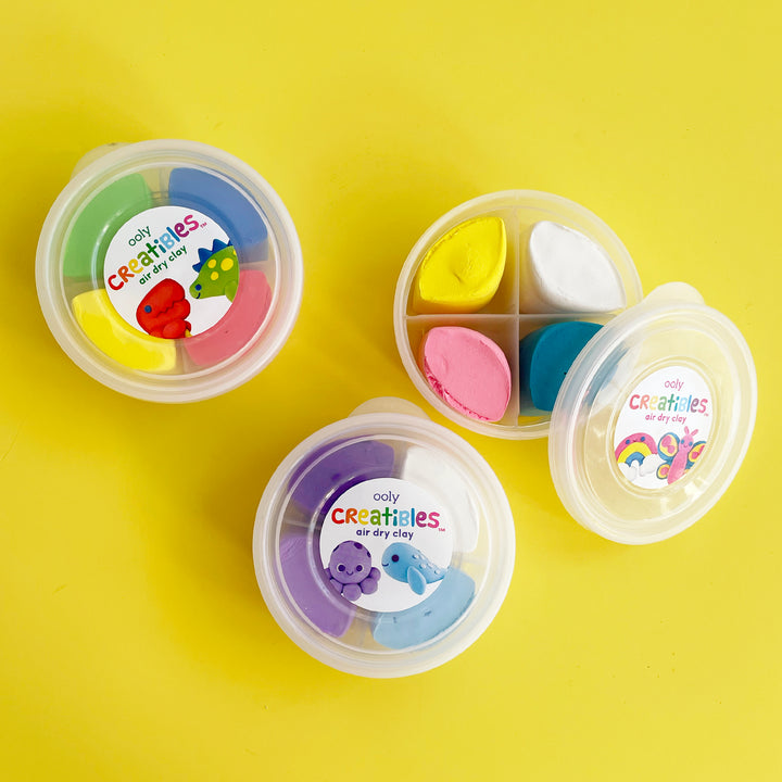 Three round containers filled with colorful air dry clay displayed on a bright yellow background.