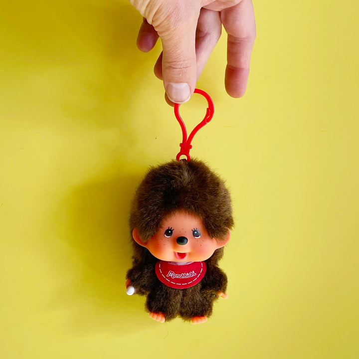 Monchhichi-shaped keychain with a red clip on a yellow background
