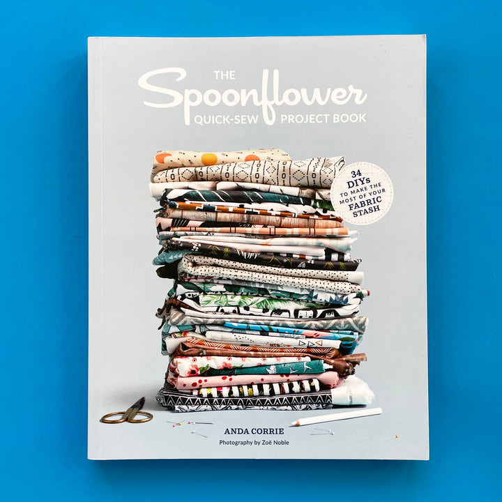 A book laying flat on a blue background. The book cover features a stack of multi colored printed fabrics folded on a light gray background.