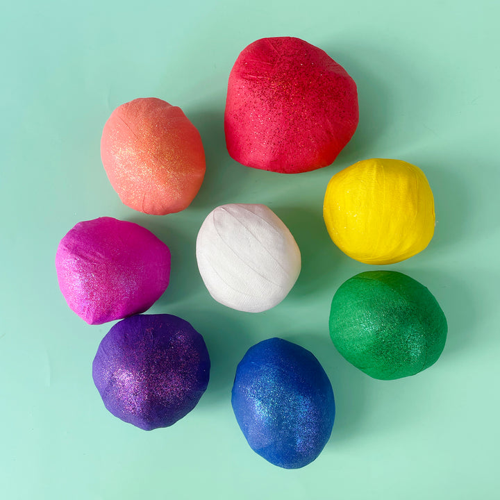 A rainbow of small surprise balls organized in a circle on a light green background.
