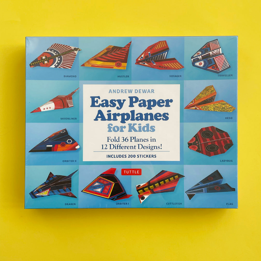 Packaged airplane folding kit displayed on a bright yellow background. Box features photographs of 12 colorful paper airplanes that can be made with the kit.