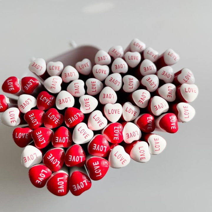 Dozens of heart shaped pencils on  a white background. The ends of the pencils say "love"