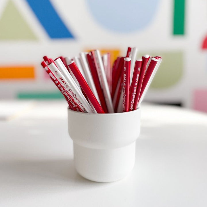 A white cup filled with red and white heart shaped pencils.