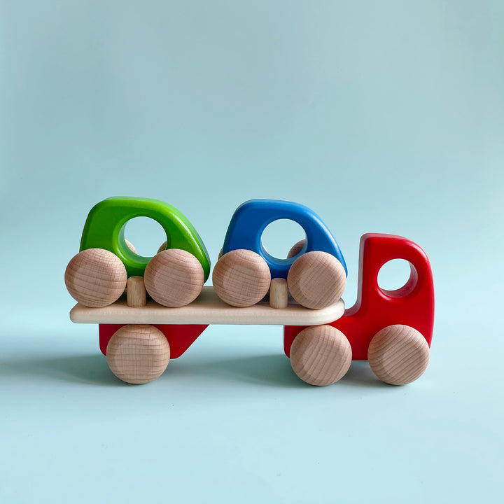 Small red wooden truck toy carrying two smaller wooden cars.