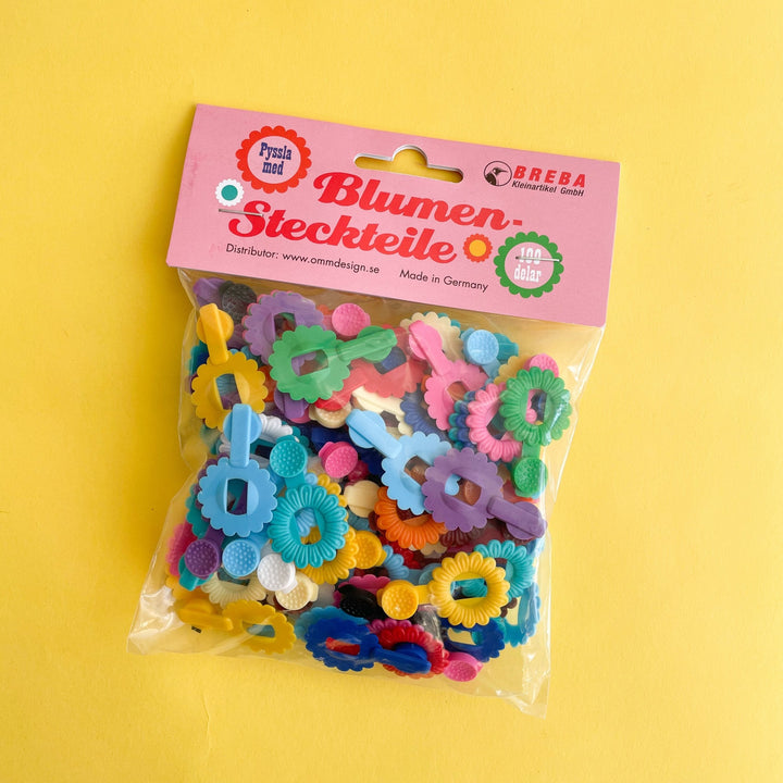 Package of multi colored  Breba flower  clips on a yellow background.