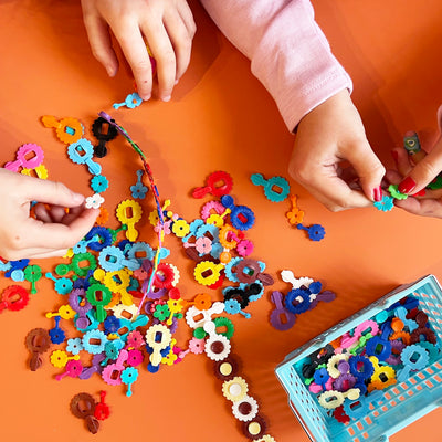 Children's hands playing with colorful plastic flower clips on an orange background
