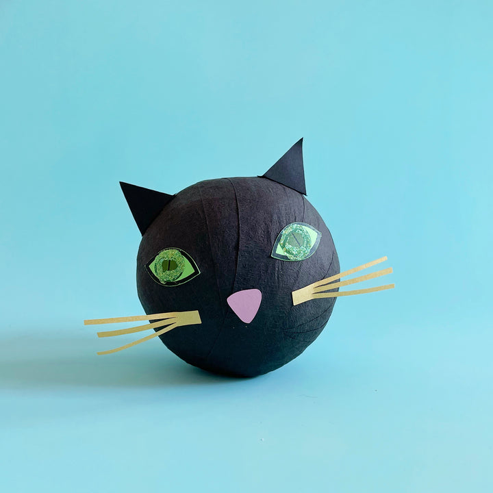 A black cat inspired surprise ball with colorful paper features and glitter details against a ligt blue background
