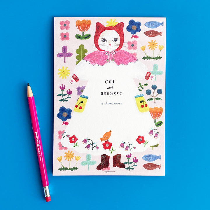 Cat and onepiece notebook on a blue background. A pink pencil lays next to it.