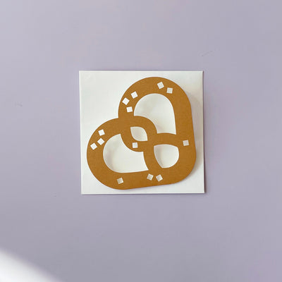 A brown pretzel shaped greeting card sitting on top of a white envelope. 