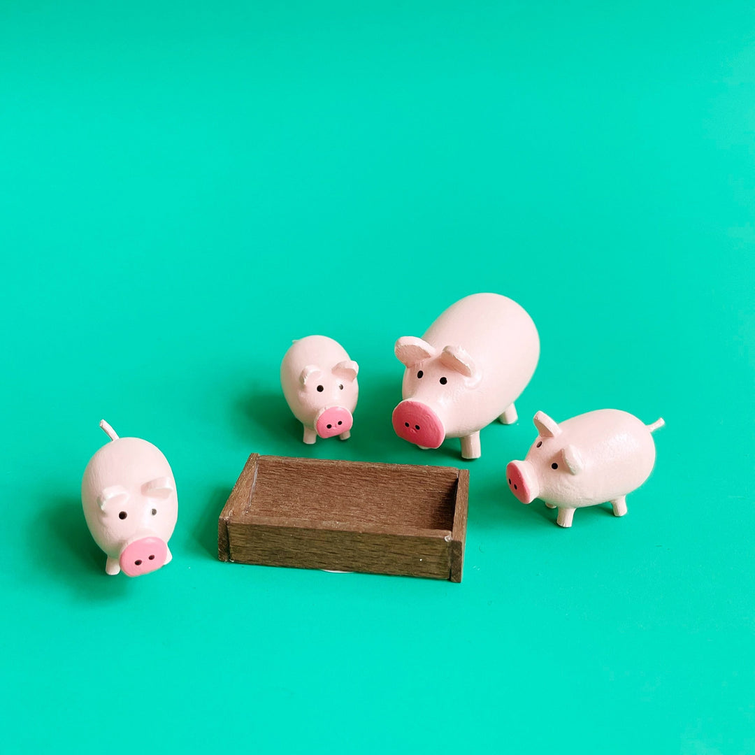 4 small wooden pigs and a trough on a green background.
