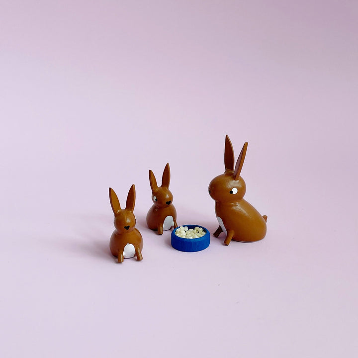 Three small  brown wooden bunny figurines on a light pink background.